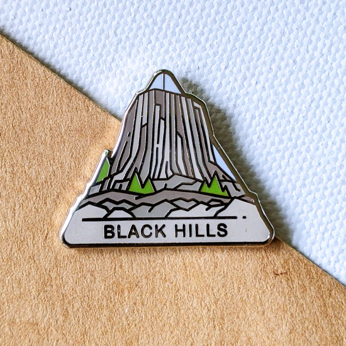 Triangle Black HIlls enamel pin featuring a view of Bear Lodge formation also known as Devil's Tower.