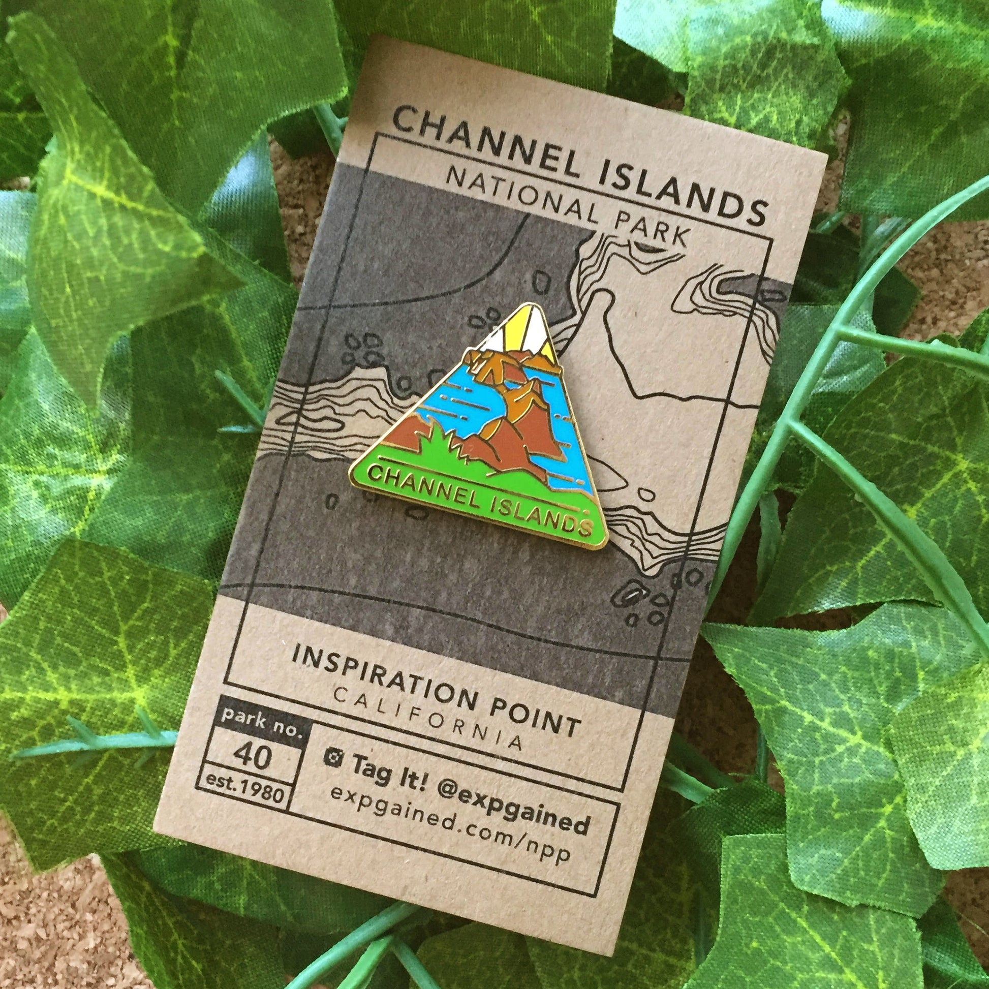 Triangle Channel Islands national park enamel pin featuring a view from the beehive hike on a brown business card size backing card with a topo map of the Anacapa Island.