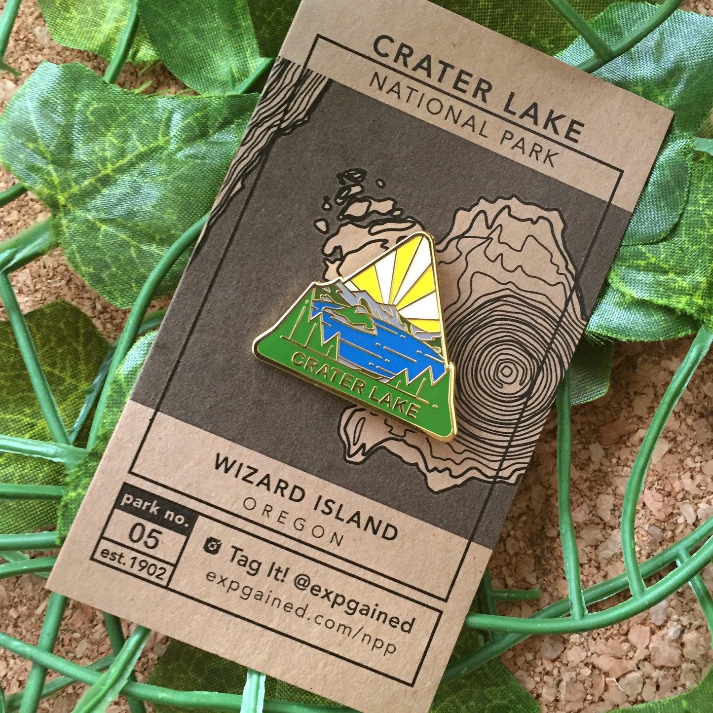 Triangle Crater Lake national park enamel pin featuring a view from the beehive hike on a brown business card size backing card with a topo map of the Wizard Island location.