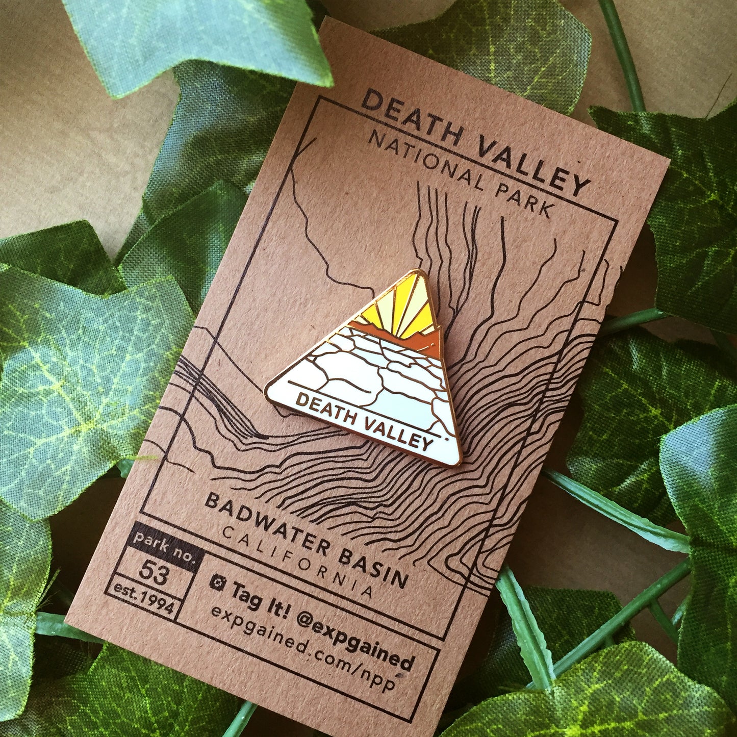 Triangle Death Valley national park enamel pin featuring a view from the beehive hike on a brown business card size backing card with a topo map of the Badwater Basin location.
