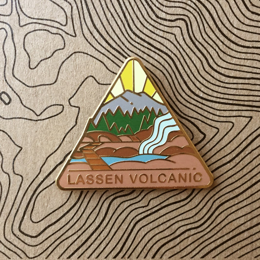 Triangle Lassen Volcanic national park enamel pin featuring a view of mount lassen and hot springs.