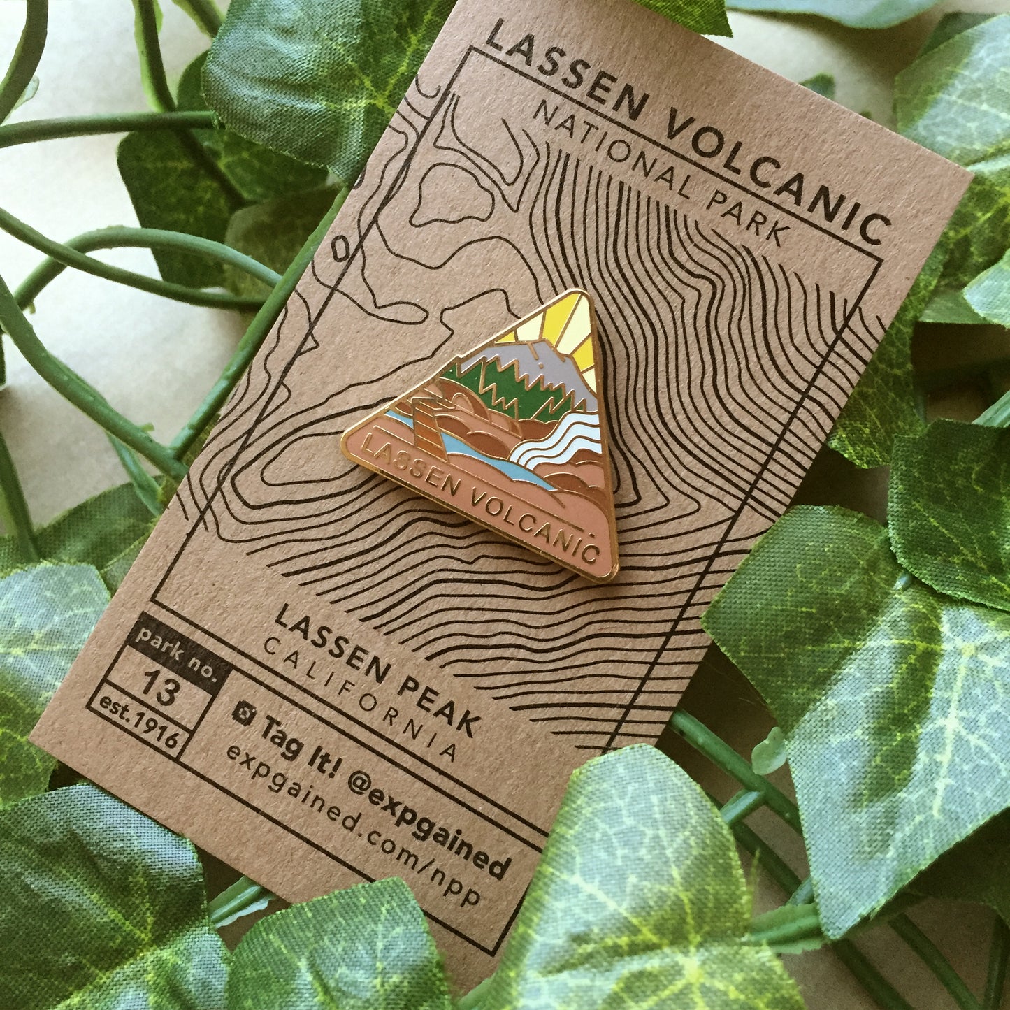 Triangle Lassen Volcanic national park enamel pin featuring a view from the beehive hike on a brown business card size backing card with a topo map of Lassen Mountain.