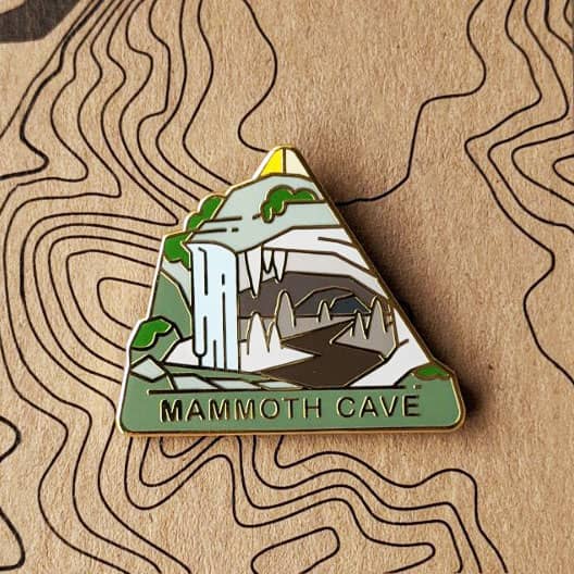 Triangle Mammoth Cave national park enamel pin featuring a view of an entrance to the cave with a waterfall.