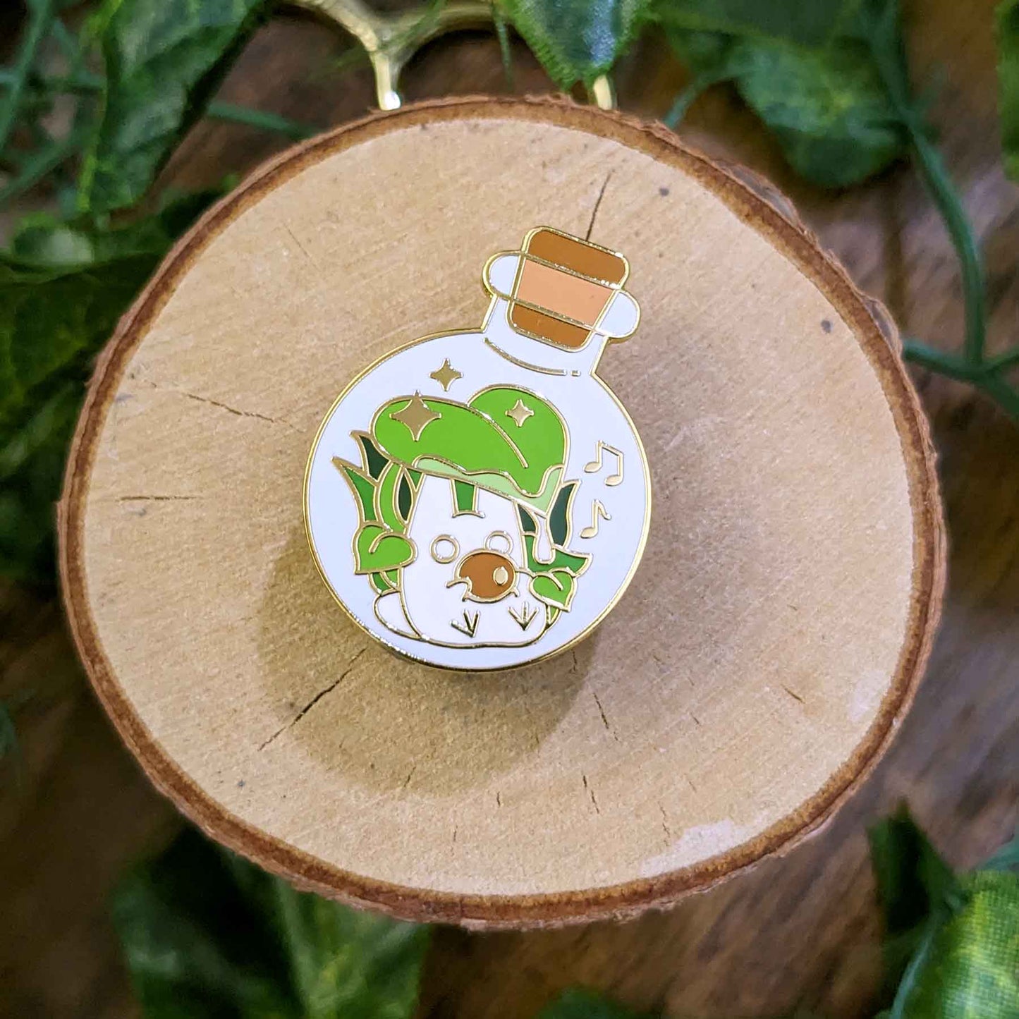 Cute white rabbit playing music with an oval instrument under a green leaf in a potion bottle enamel pin designed by EXP Gained