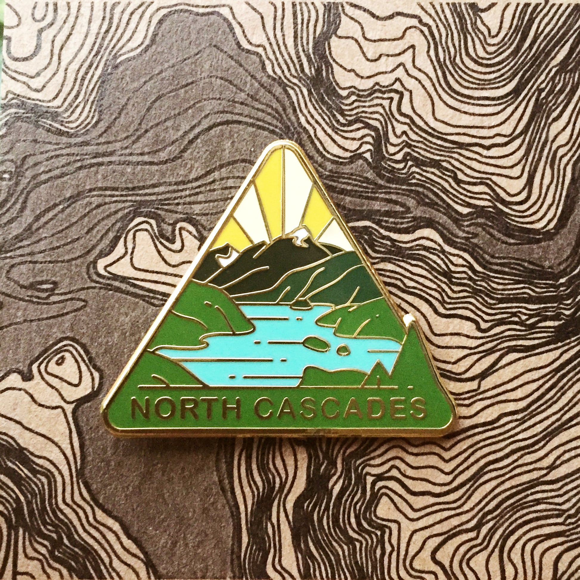Triangle North Cascades national park enamel pin featuring a view of Diablo Lake.