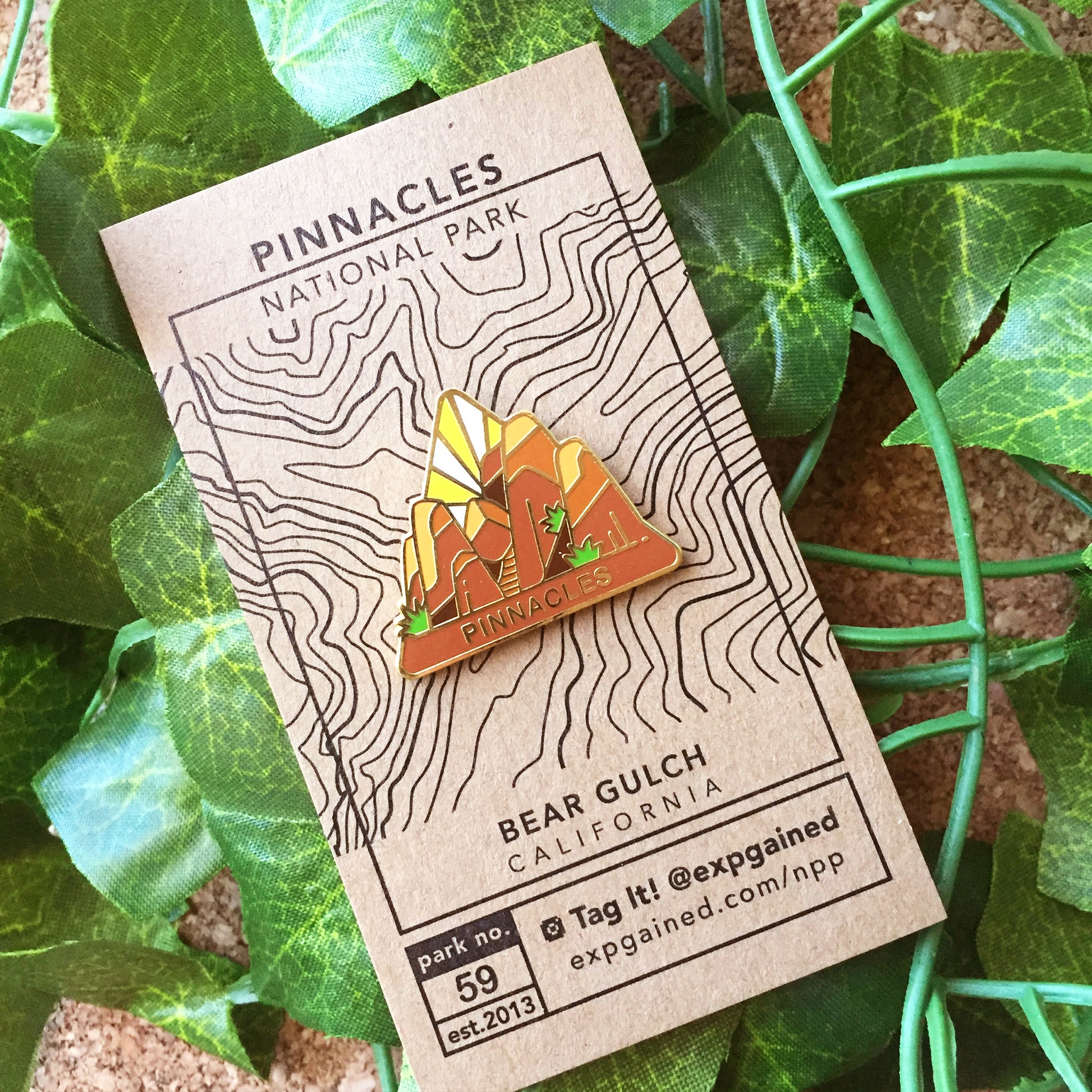 Triangle Pinnacles national park enamel pin featuring a view from the beehive hike on a brown business card size backing card with a topo map of the Bear Gulch trail.