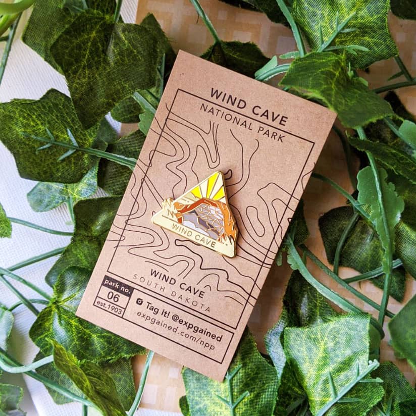 Triangle Wind Cave national park enamel pin featuring a view from the beehive hike on a brown business card size backing card with a topo map of the Wind Cave location.