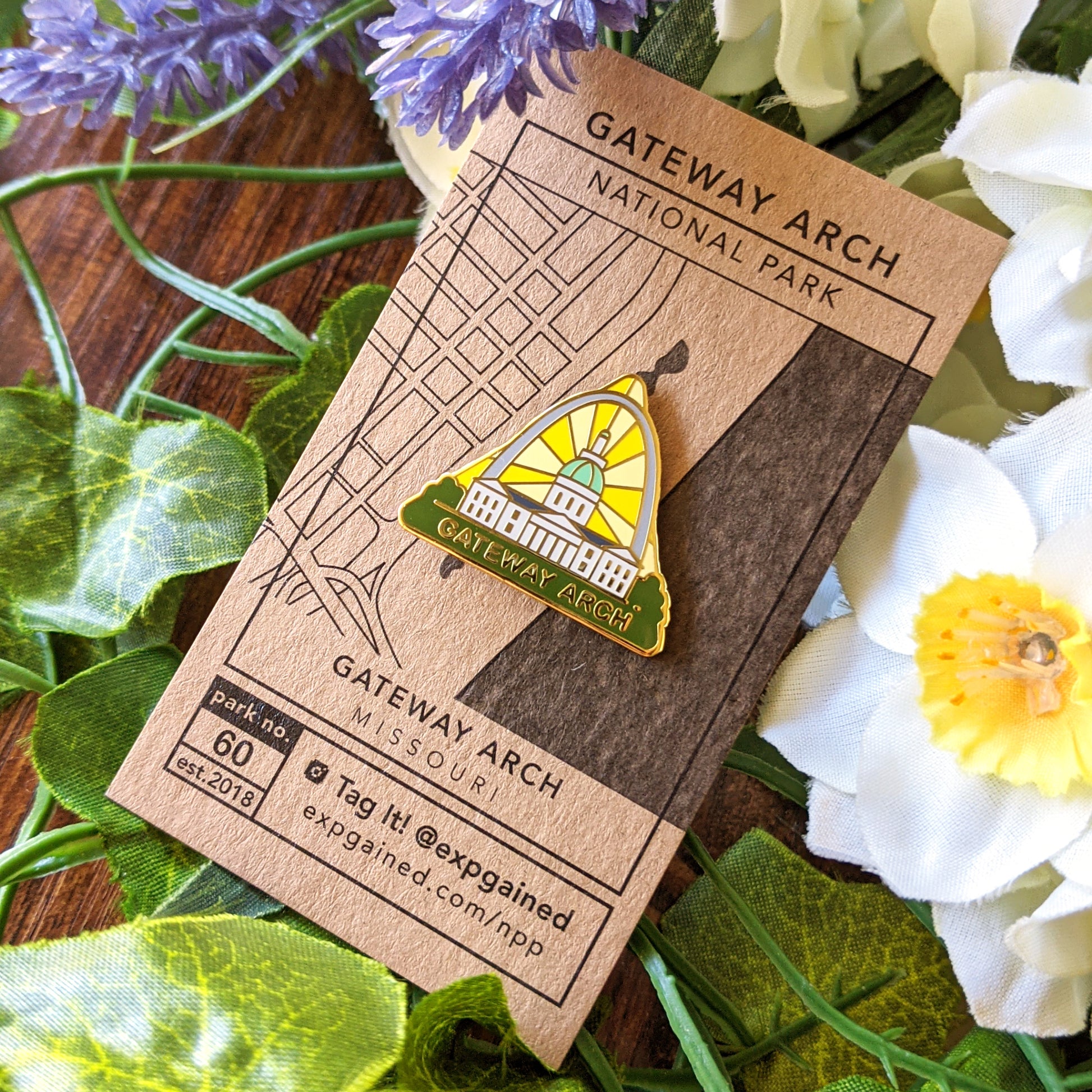 Triangle Gateway Arch national park enamel pin featuring a view from the beehive hike on a brown business card size backing card with a topo map of the arch and capitol building.