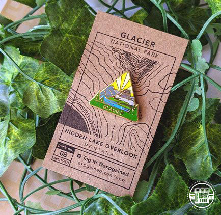 Triangle Glacier national park enamel pin featuring a view from the beehive hike on a brown business card size backing card with a topo map of the Hidden Lake Overlook.