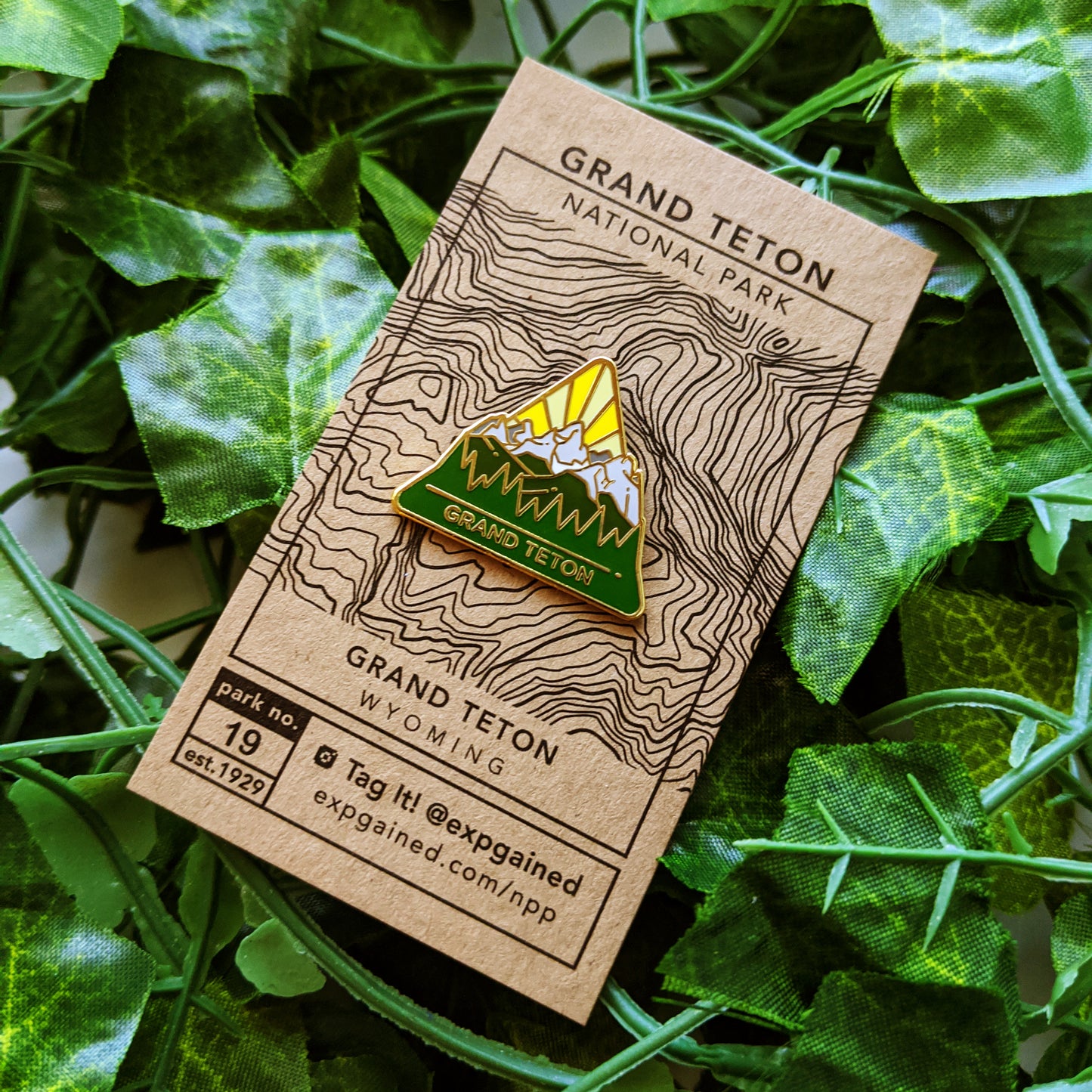 Triangle Grand Teton national park enamel pin featuring a view from the beehive hike on a brown business card size backing card with a topo map of the teton range.