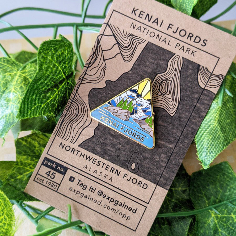 Triangle Kenai Fjords national park enamel pin featuring a view from the beehive hike on a brown business card size backing card with a topo map of the Northwestern Fjord.