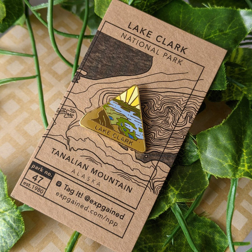 Triangle Lake Clark national park enamel pin featuring a view from the beehive hike on a brown business card size backing card with a topo map of Tanalian Mountain.