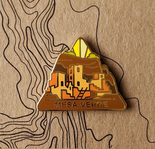 Triangle Mesa Verde national park enamel pin featuring a view of cliff dwellings.