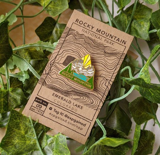 Triangle Rocky Mountain national park enamel pin featuring a view from the beehive hike on a brown business card size backing card with a topo map of Emerald Lake.