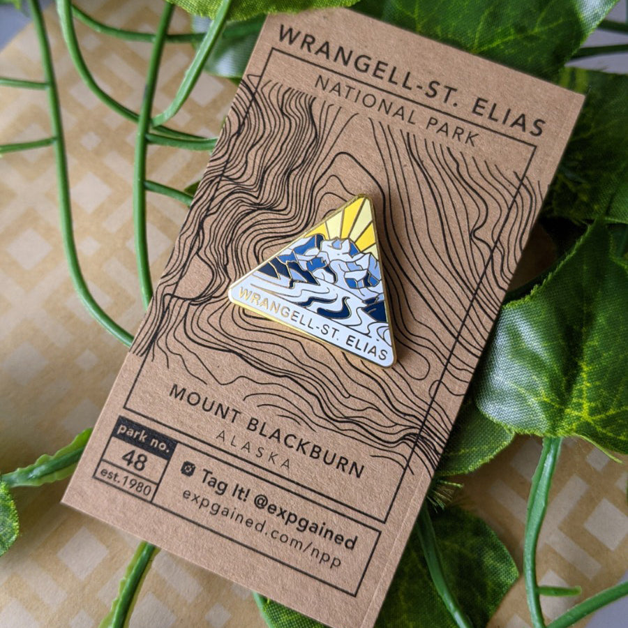 Triangle Wrangell-St. Elias national park enamel pin featuring a view from the beehive hike on a brown business card size backing card with a topo map of Mount Blackburn.